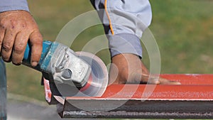 Close-up of man in working clothes cutting a list of red steel roofing by metal cutting saw. Clip. Materials and