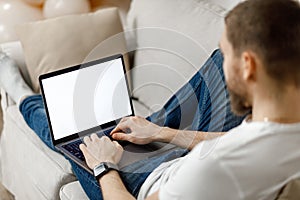 close-up of a man working on a laptop at home on the couch. no face