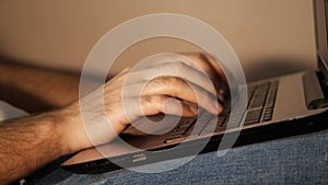 Close-up of a man& x27;s hands typing on a laptop that lies on his lap. Remote work at the laptop in the evening. Side
