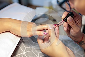 Close-up of manicurist applying red nail polish
