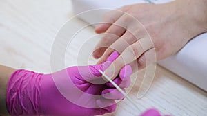 Close-up of a manicurist hand applying a nail polish to a man fingernail. A man doing a manicure in the beauty salon