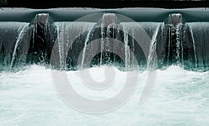 Close up of a manmade concrete weir in a city with a blue river cascading over it