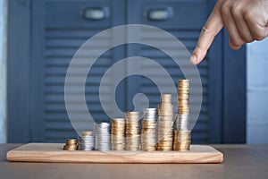 Close-up of a mans hand pointing at columns of multi-colored coins of increasing height, concept of saving and saving money,