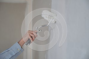 Close-up of mans hand using paint roller with white paint.