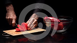 Close up of mans hands chopping tomato on black background