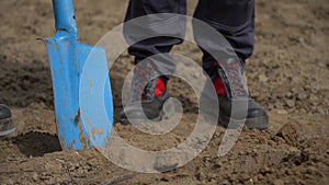 close up of mans hands in gloves and digging a shovel in the garden