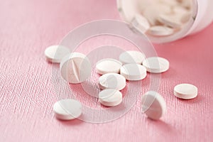 Close up of many while color medical pills spilling on pink
