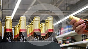 Close-up of many glass beer bottles in golden foil and a male buyer examines and takes a couple