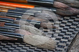 Close-up of many multicolored brushes lying on a chess mat and ready to paint, selective focus