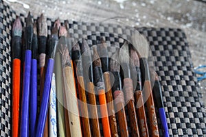 Close-up of many multicolored brushes lying on a chess mat and ready to paint, selective focus