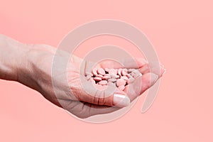 Close-up of many pink pills in woman hand on pink background. Medical concept of medicine treatment, vitamins