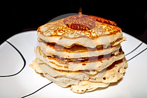 Close up of Maple syrup pouring onto fluffy hotcakes on a white plate.