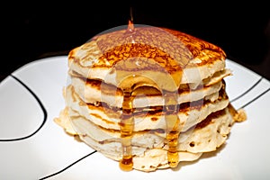 Close up of Maple syrup pouring onto fluffy hotcakes on a white plate. photo