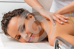 Close-up massage and body care in spa salon for young woman, beautiful happy girl with closed eyes enjoying treatment procedure,
