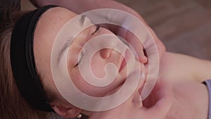 Close up of masseuse hands massaging female face. Woman closed eyes with pleasure.