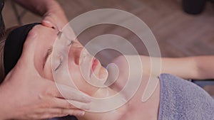 Close up of masseuse hands massaging female face. Woman closed eyes with pleasure.