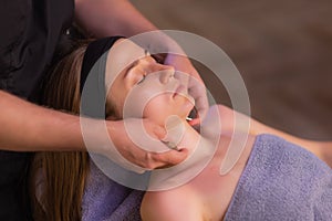 Close up of masseuse hands massaging female face. Woman closed eyes with pleasure.