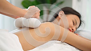 Close up of masseuse hands use hot compress treatment in Thai spa on her back. Woman get a therapy massage for full body.