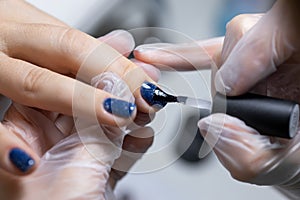 Close-up, the master evens the color of the manicure with blue, applying gel polish on it with a brush