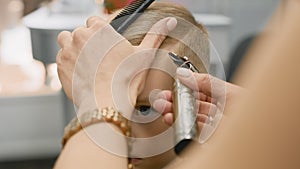 Close-up of master makeup artist with an electric trimmer cuts child's hair. Hairdresser cuts strip of parting