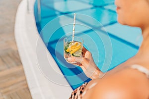 Close up of mature adult woman holding cocktail and relaxing near the pool. Beautiful elegant caucasian senior woman