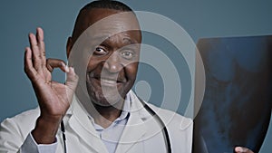 Close-up mature african american man doctor surgeon traumatologist radiologist in medical coat in studio blue background