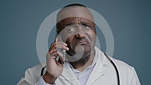 Close-up mature african american man talking mobile phone in studio gray background confused puzzled doubting male
