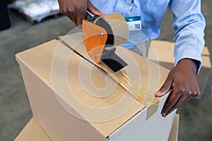 Male staff packing cardboard box with tape gun dispenser in warehouse