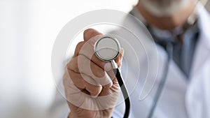 Close up mature doctor holding stethoscope, medical checkup photo