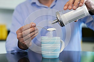 Close Up Of Mature Man Adding Sugar To Hot Drink At Home