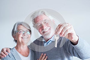 Close up of mature man holding a key of a new home or house or some property of both - couple of seniors and pensioners smiling