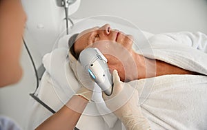 Close-up of a mature man relaxing during beauty procedure at wellness spa centre while aesthetician doing face lifting anti-aging