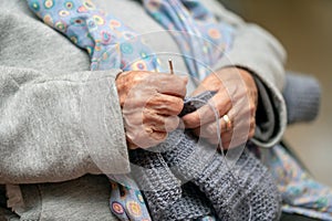 Close up of a mature woman knitting at home, enjoying leisure time, holding needles, elderly generation hobby activity.