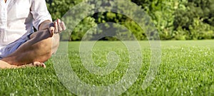 Close up of mature woman meditating on green meadow in the park.