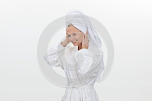 Close-up of a mature woman in a white bathrobe with a towel on her head applies