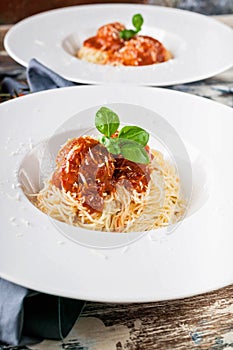 Close-Up meatballs in tomato sauce with spaghetti on white plates, cherry tomatoes on a wooden table