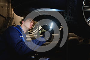 Close-up of a mechanic, technician, auto engineer checks the underbody of the car with flashlight in the garage of a repair shop.