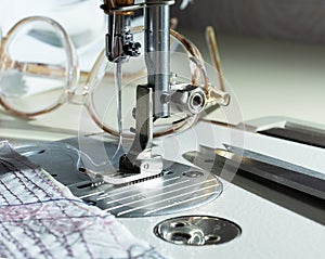 close-up of mechanism with a needle of an electric sewing machine. against the background of glasses and fabric with