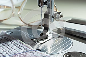 close-up of mechanism with a needle of an electric sewing machine. against the background of glasses and fabric with