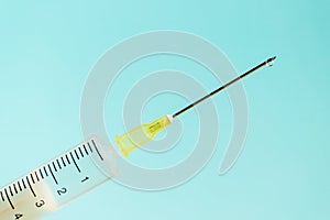 Close up of a medical syringe with a drop of drug or medicine at the end of needle on a blue background