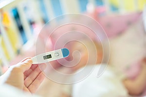 Close-up medical thermometer, Parent measuring temperature of ill kid, 1 years old toddler girl gets high fever lying on bed.