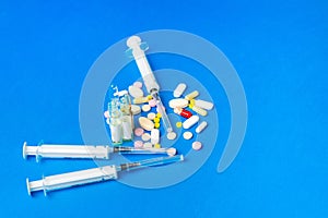 Close up medications, tablets, ampoules and syringe on blue background. Concept of treatment of influenza and viruses. Copy space