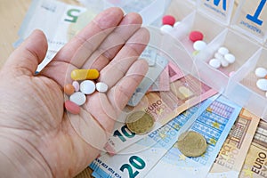 close-up medicinal capsules, pills, vitamins in female palm, plastic pillbox organizer for week, euro banknotes, concept