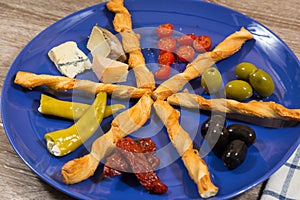 close up of mediterranean antipasti plate with two kinds of olives tomatoes cheese filled peppers separated by breadsticks