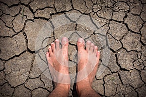 Close up of men feet on dry cracked earth texture for background, top view global warming concept