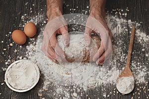 Close-up of men`s baker hands on black bread with flour powder. Baking and patisserie concept