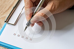 Close- up, Men`s fingers holding pen writing on checklist paper and the format for filling in information in business concept.