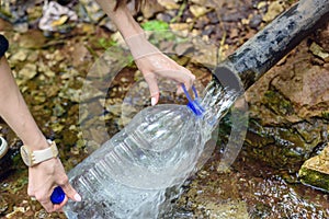 Close-up of men`s hands with a plastic bottle, fills with clean fresh water from the spring, underground source