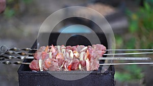 Close up of men's hands puts skewers with raw shashlik and vegetables on chargrill. Succulent barbecue with onions and