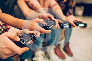 Close up of men and women hands holding joysticks. THey sit together in one row. Play intense game. Cut view.